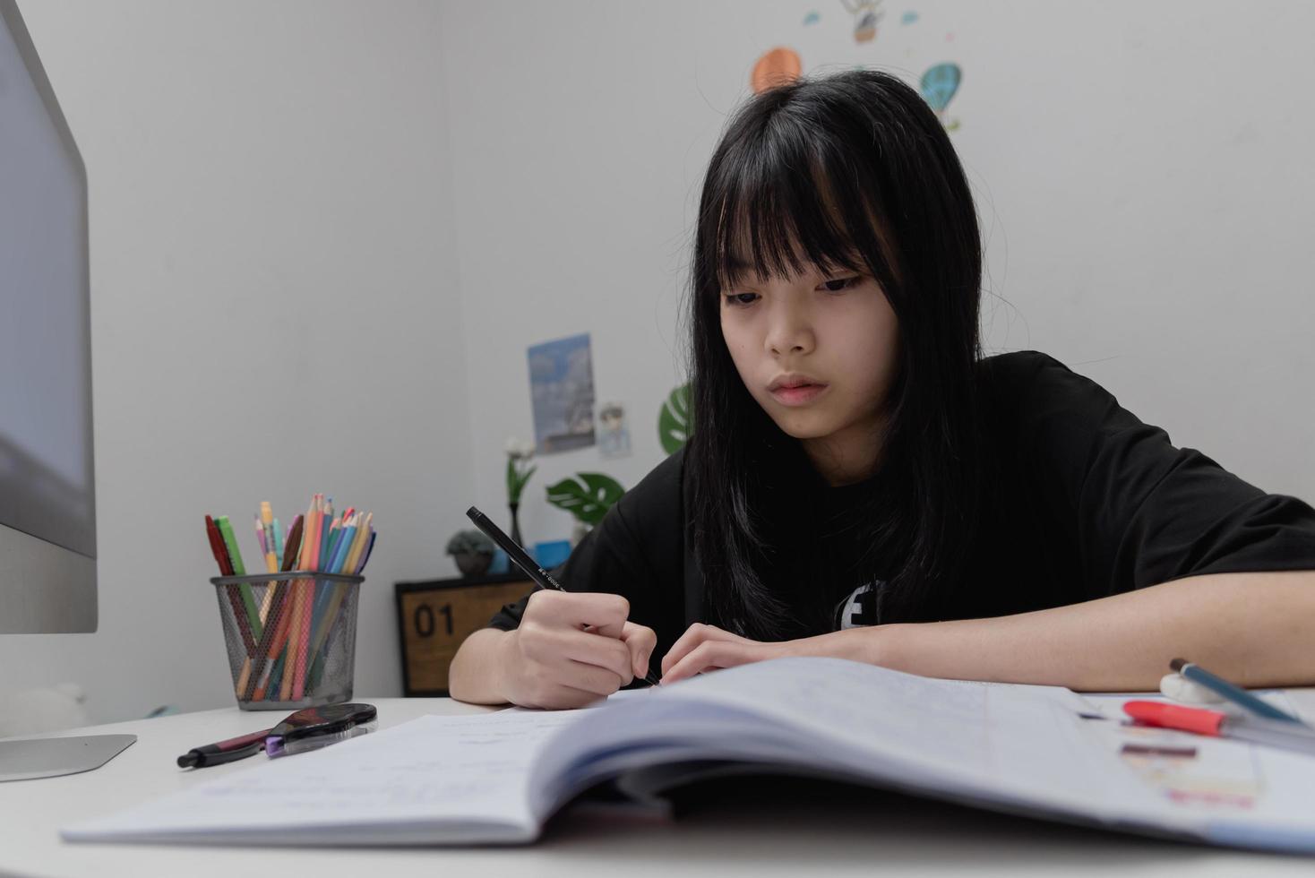 asiatische studentin schreibt hausaufgaben und liest buch am schreibtisch foto