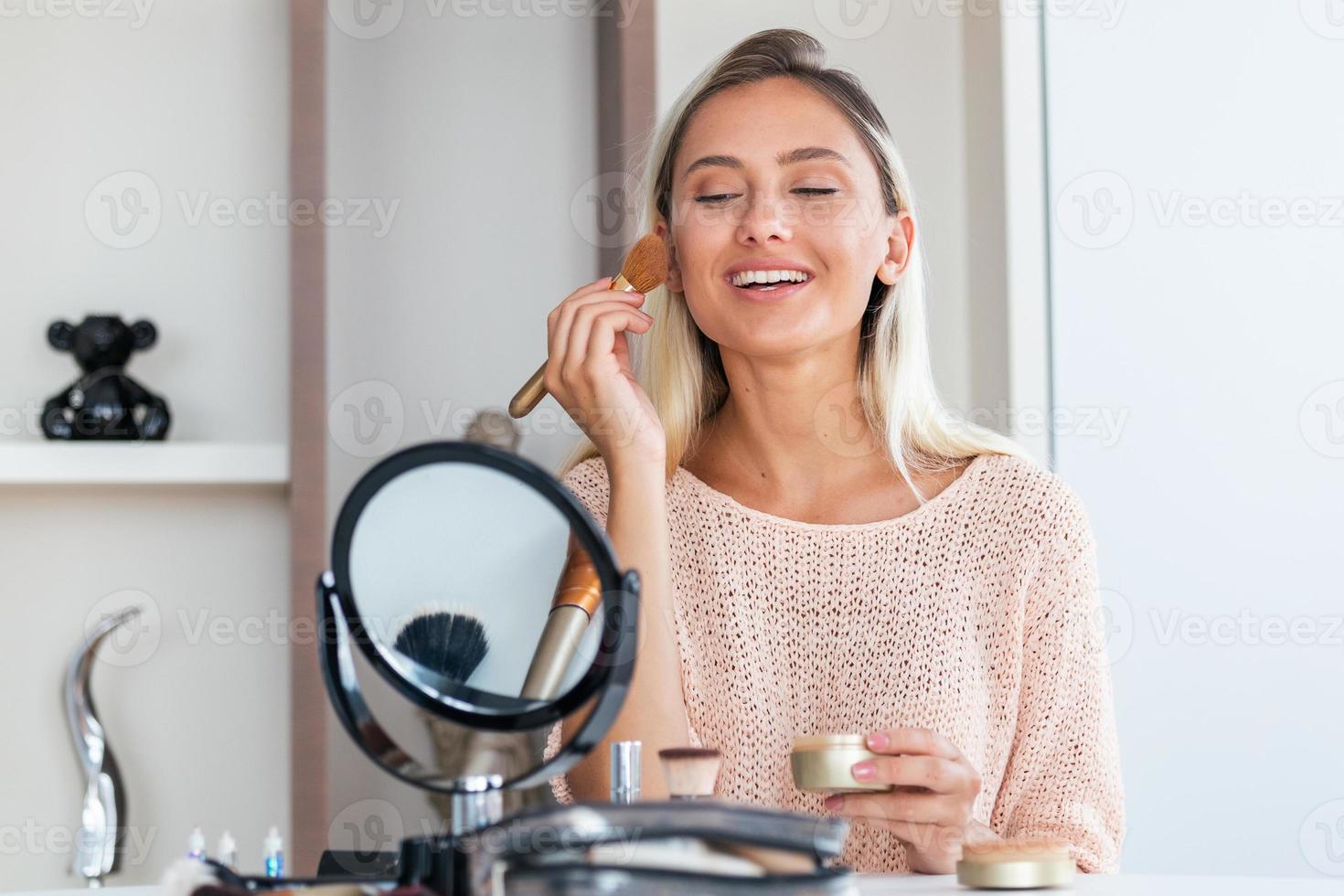 Schönheitsfrau, die Make-up anwendet. Schönes Mädchen, das in den Spiegel schaut und Kosmetik mit einem großen Pinsel aufträgt. Mädchen wird auf den Wangenknochen rot. Puder, Rouge foto