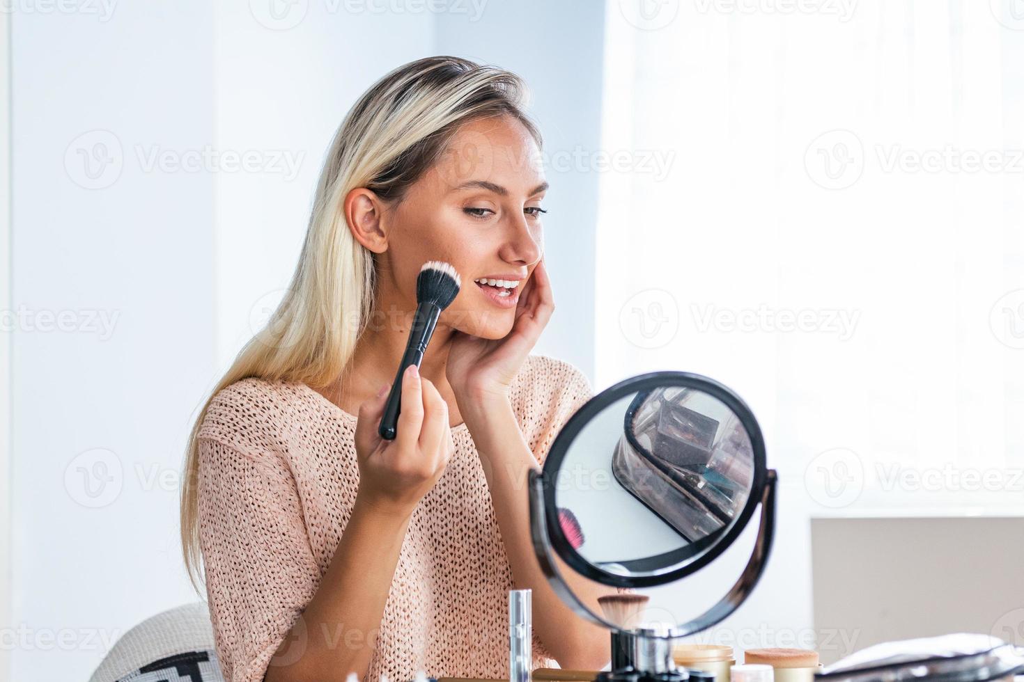 junge schöne frau, die ihr make-up aufträgt und in einen spiegel schaut. schönes Mädchen mit kosmetischem Puderpinsel zum Schminken. bilden. Schminken für perfekte Haut. foto