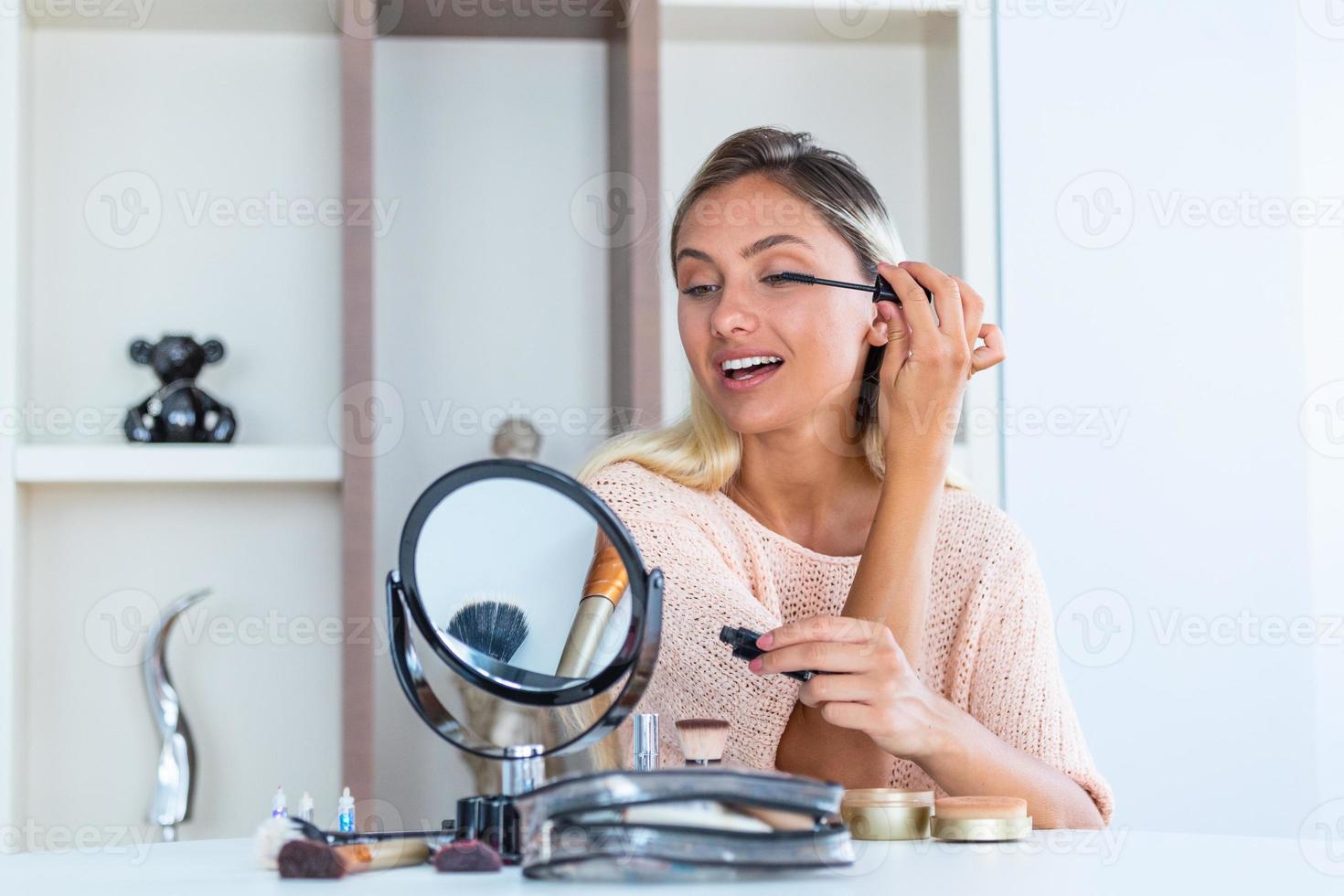 Schöne Frau, die Make-up aufträgt, malt ihre Wimpern für ein abendliches Date vor einem Spiegel. Porträt einer schönen jungen Frau, die schwarze Wimperntusche auf die Wimpern aufträgt und eine Bürste in der Hand hält. foto