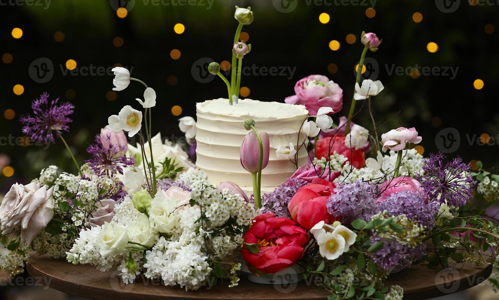 Weiße Hochzeitstorte mit frischen Rosen und wilden Blumen im Freien. Hochzeitsdeko Tisch im Garten, Blumenarrangement, im Stil Vintage. Hochzeitsfeier foto