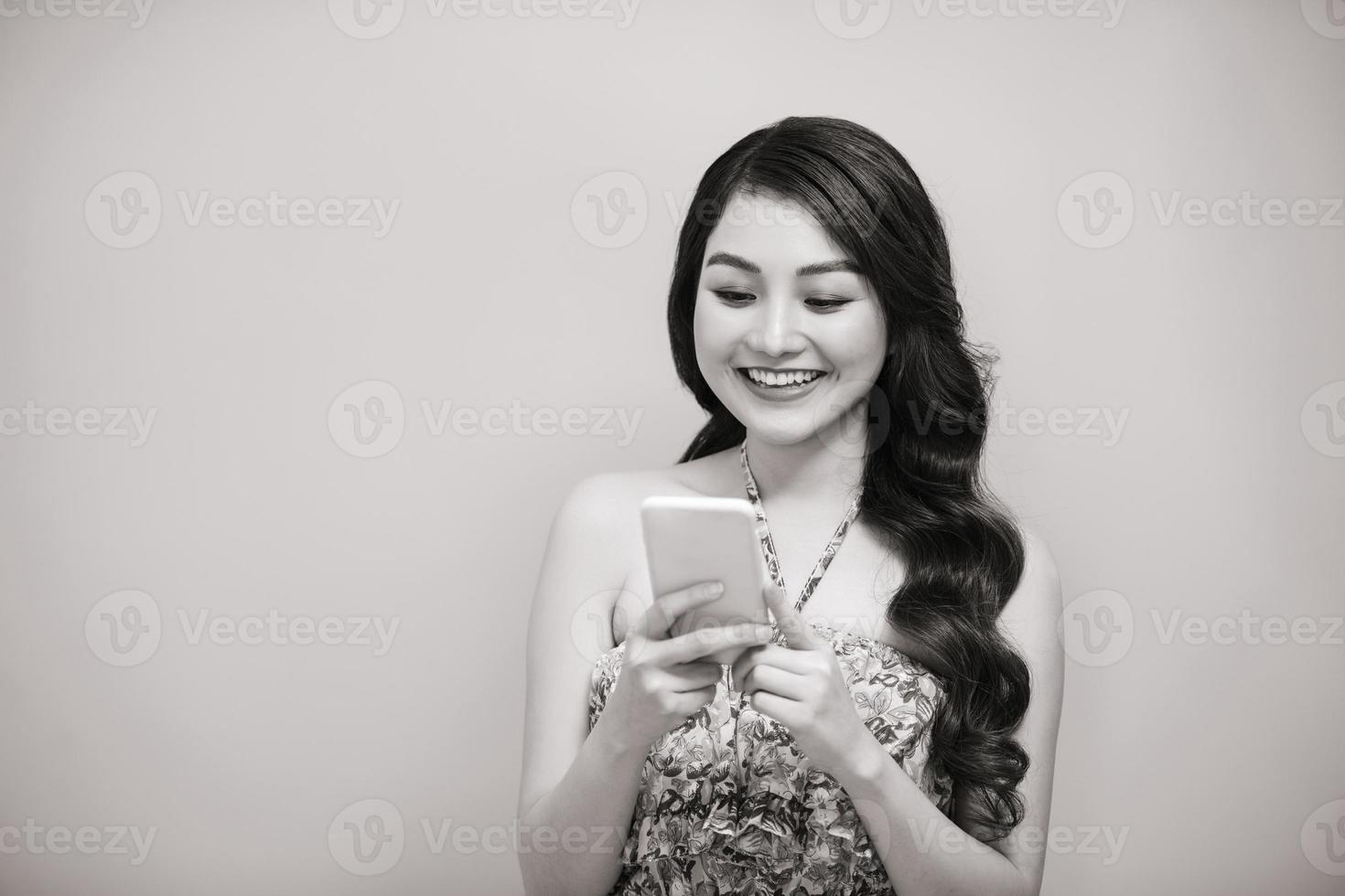 Porträt einer lächelnden lässigen Frau, die Smartphone über weißem Hintergrund hält. Schwarz-Weiß-Foto. foto