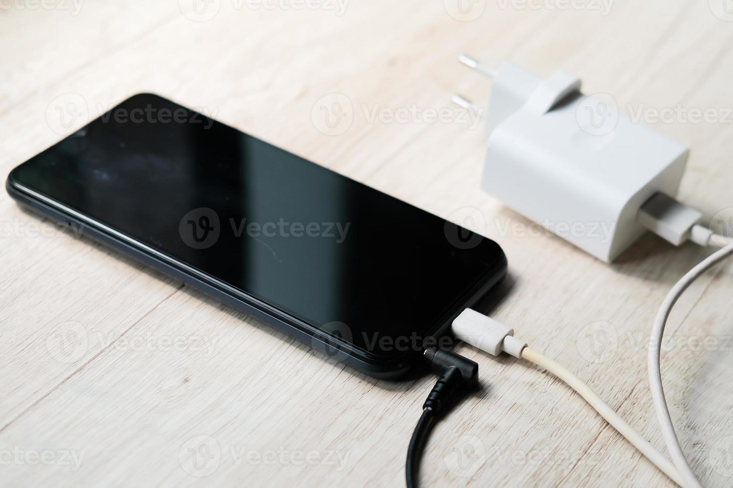 Modernes Smartphone mit eingesteckten Strom- und Audiokabeln auf dem Tisch foto