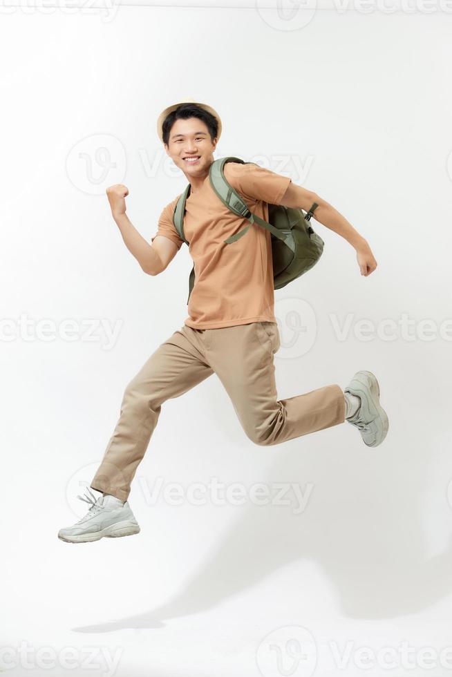 Reise-, Tourismus- und Personenkonzept - glücklicher lächelnder junger Mann mit dem Rucksack, der über weißem Hintergrund in die Luft springt foto