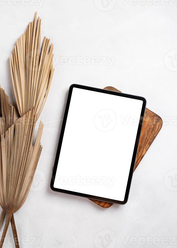 digitaler Tablet-Computer mit isoliertem Bildschirm auf dem Schreibtisch. zu hause innenraum mit palmblättern foto
