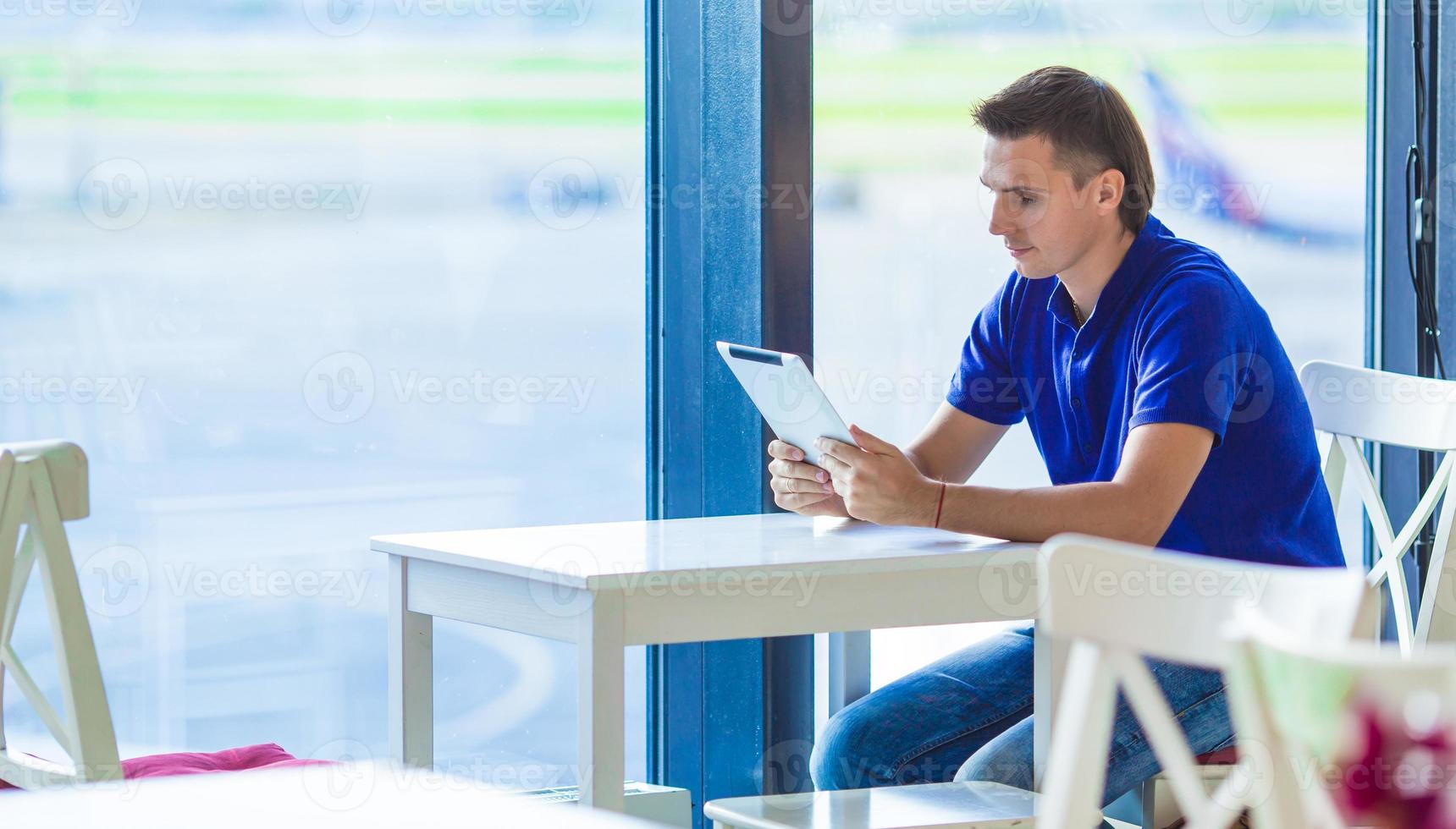 junger Mann am Flughafencafé beim Warten auf das Einsteigen foto