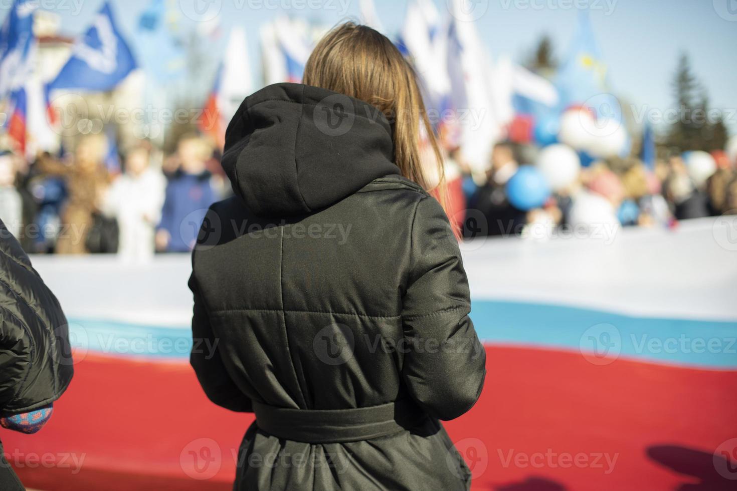 Mann bei Rallye in Russland. Mädchen steht vor dem Hintergrund von Menschen mit Flaggen Russlands. foto