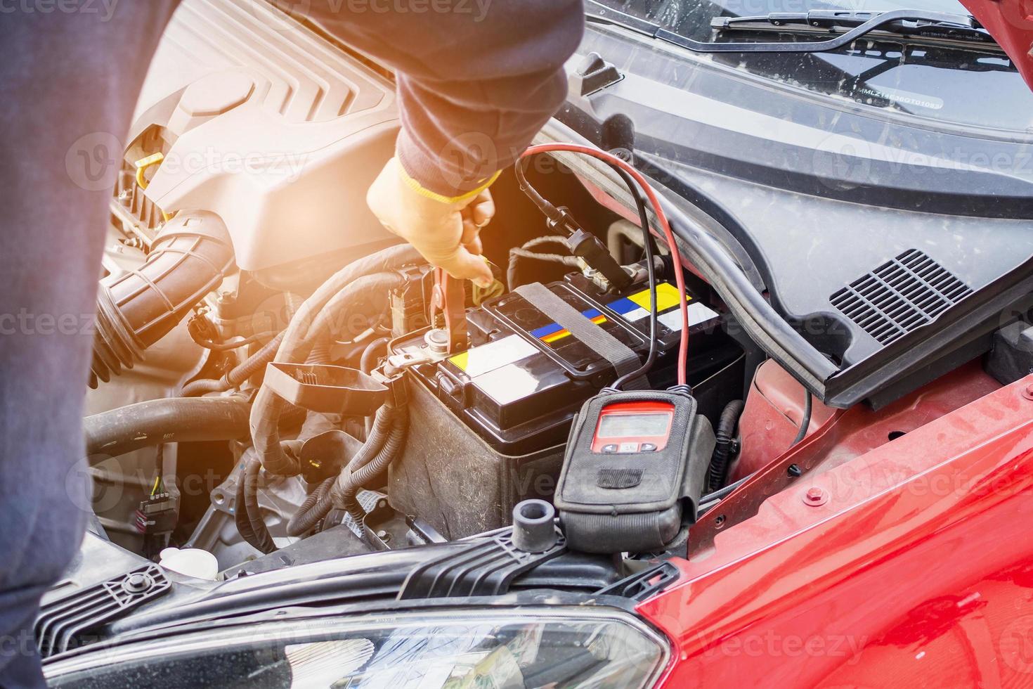 automechaniker verwenden voltmeter, um den spannungspegel der autobatterie zu überprüfen foto