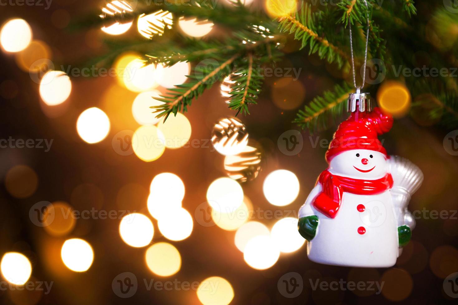 weihnachtsspielzeug schneemann in einem roten hut mit einem schal auf einem lebenden zweig einer tanne mit goldenen lichtern von girlanden in defokussierung. neujahr, weihnachten, feiertagshintergrund, bokeh, kopierraum foto