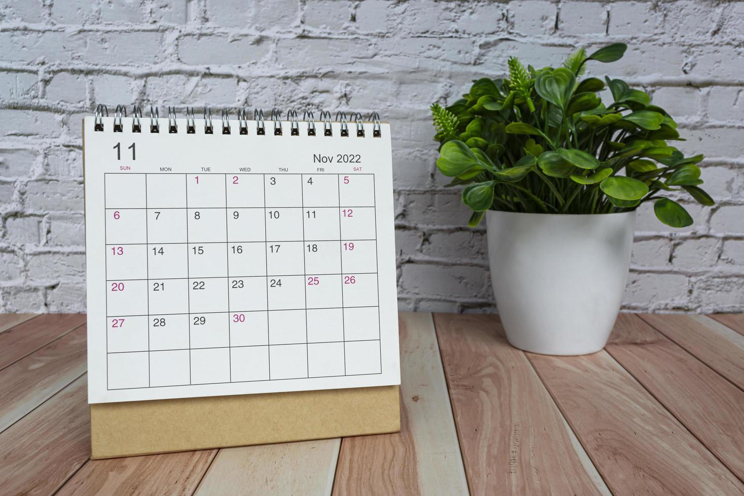 november 2022 weißer kalender mit topfpflanze auf holzschreibtisch. foto