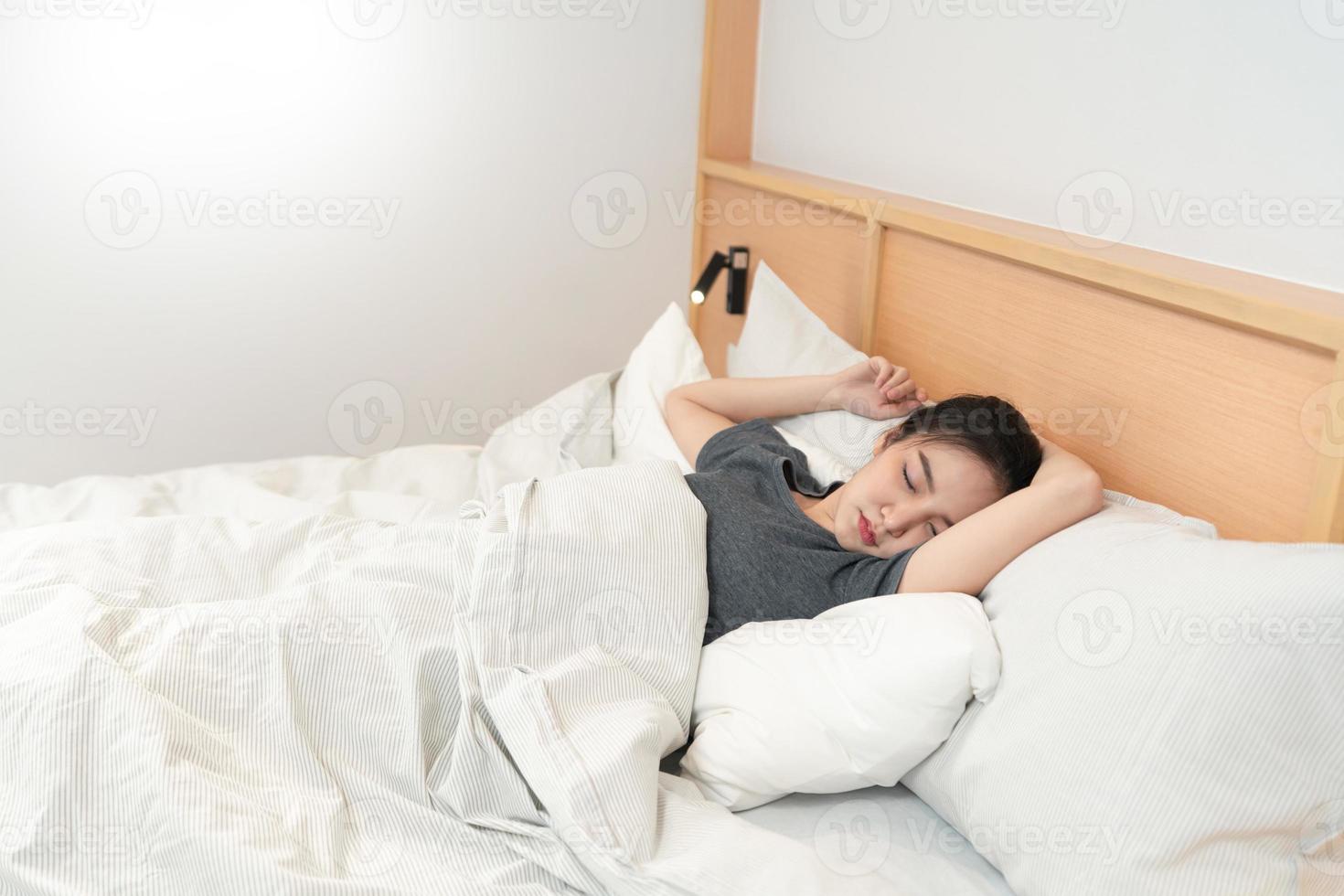 Schlafzimmerkonzept Ein Mädchen fühlt sich morgens schläfrig und liegt auf dem weißen Bett, das von der Decke bedeckt ist foto