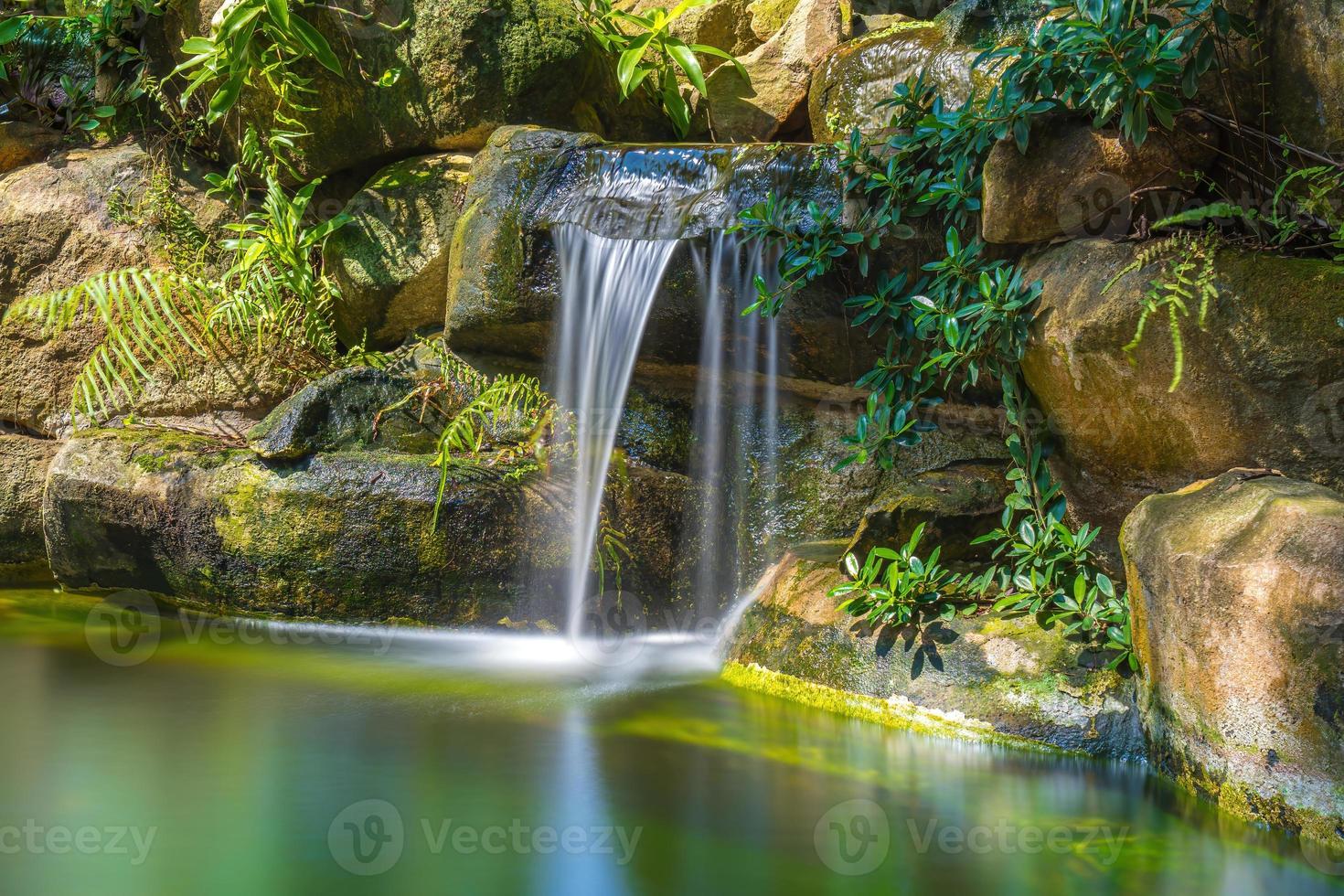 Wasserfälle im japanischen Garten. Üppig grüner tropischer Koi-Teich mit Wasserfall von jeder Seite. ein üppiger grüner Garten mit Wasserfall, der die felsigen Steine hinunterstürzt. Zen und friedlicher Hintergrund. foto