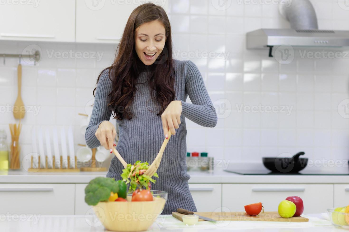 schöne, coole, schwangere frau kocht glücklich organische und gesunde salate in der modernen küche. konzept der körperpflege und vorbereitung vor der geburt foto