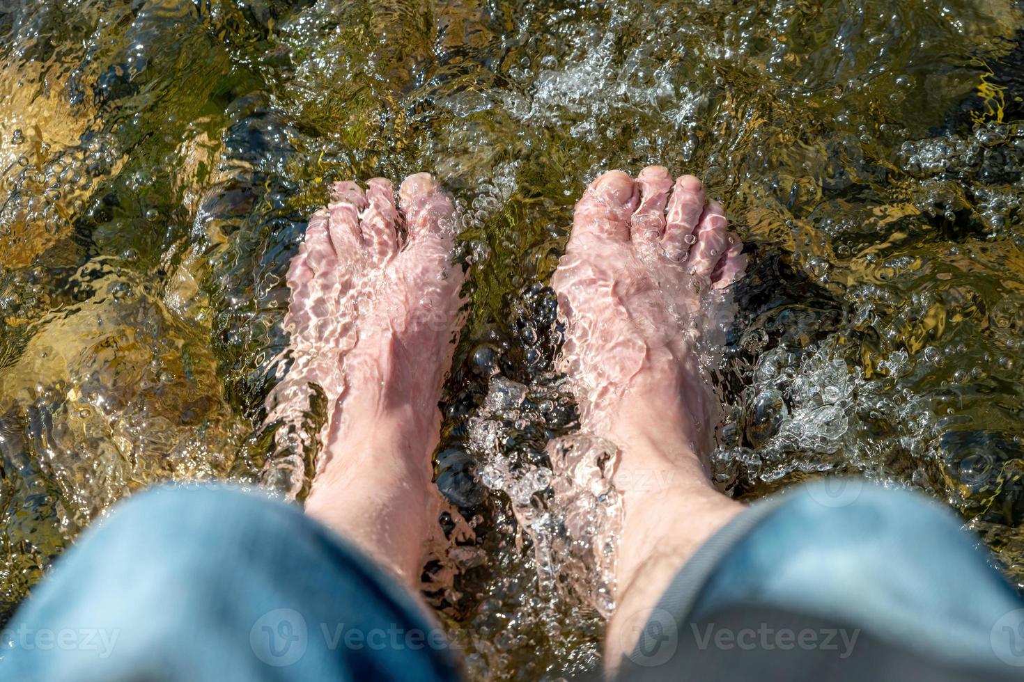 Fließendes Wasser zwischen Steinen umspült die Füße eines Mannes im Sonnenschein foto