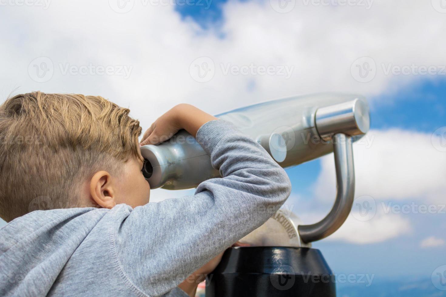 kleiner Junge, der durch ein Fernglas gegen den Himmel schaut. foto