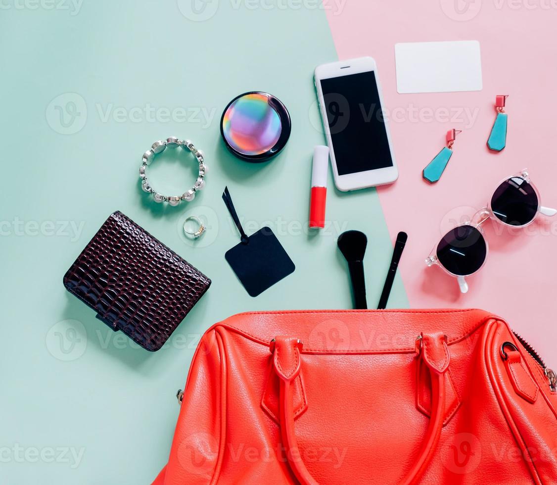 Flache Lage der rosa süßen Frauentasche mit Kosmetik, Accessoires, Tag-Karte und Smartphone auf buntem Hintergrund mit Kopierraum foto