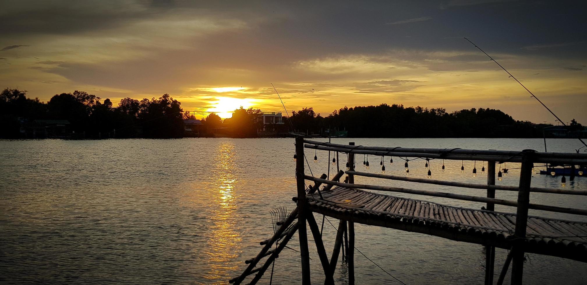 Silhouette der hölzernen Uferpromenade, Ufergegend oder Brücke mit Fluss- und Baumhintergrund bei Sonnenuntergang oder Sonnenschein. schönes natur- und freiheitskonzept. natürliche tapete mit kopierraum. foto