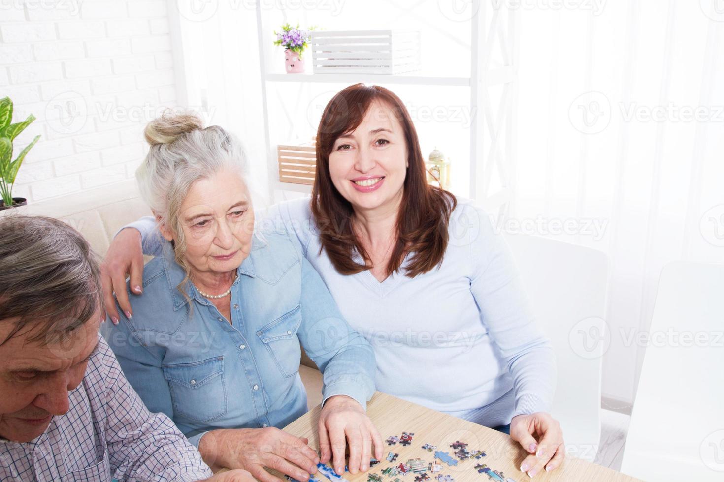 tochter umarmt ihre ältere mutter zu hause für einen selektiven fokus eines puzzlespiels foto