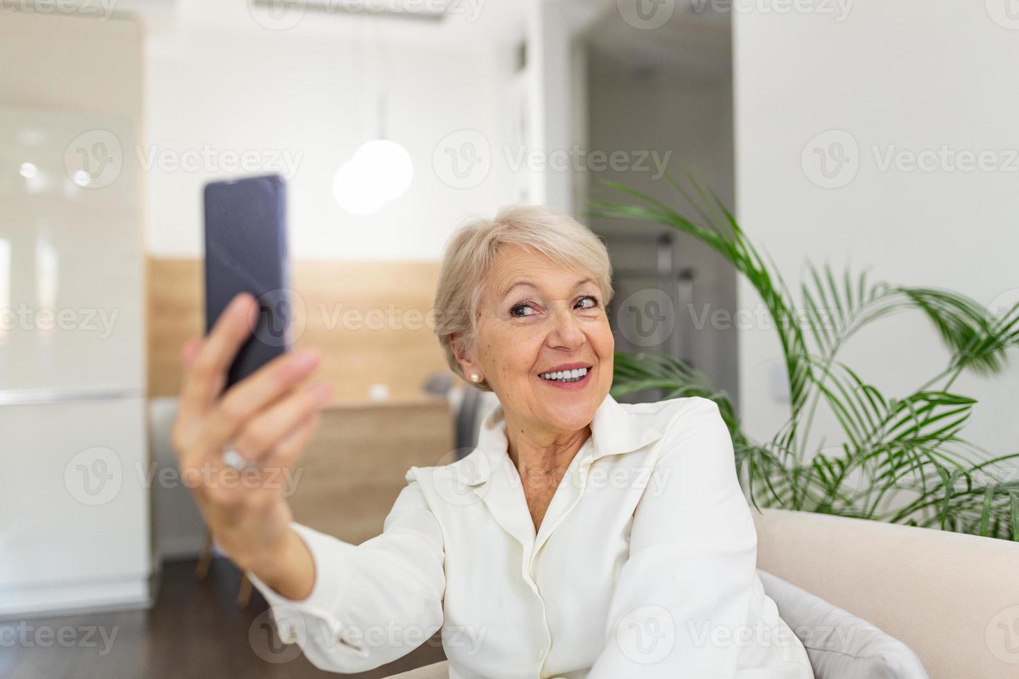 oma macht selfies zu hause im wohnzimmer. Nahaufnahme Porträt einer fröhlichen, entzückenden, charmanten, schönen älteren Dame, Oma, Oma, die ein Selfie macht. alters-, ruhestands- und personenkonzept foto