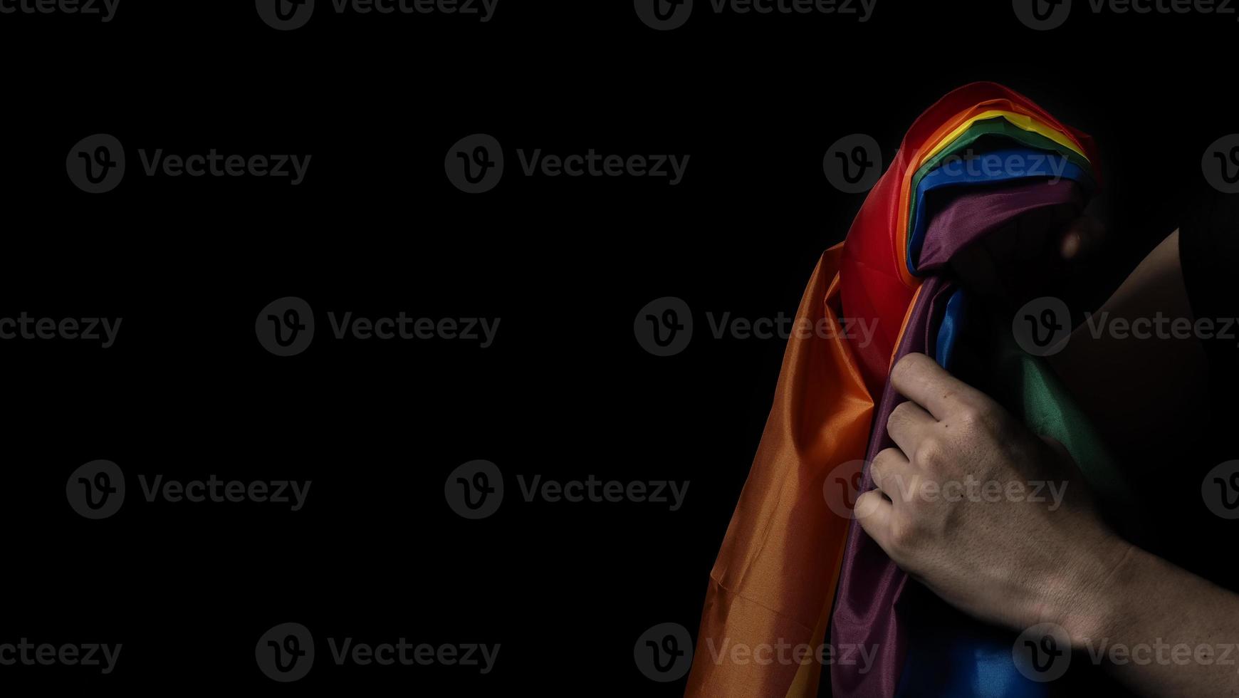 lgbtq-stolzflagge auf schwarzem hintergrund. lgbt-regenbogenfahne in schwuler hand. foto