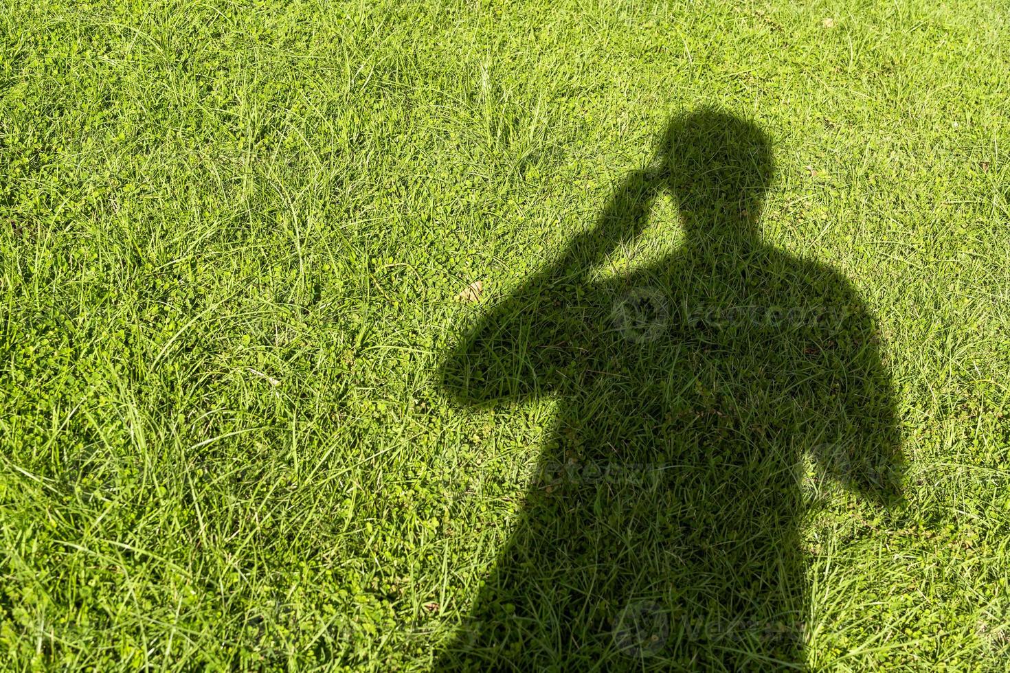 Schatten einer Person, die ein Telefon auf dem Gras benutzt foto