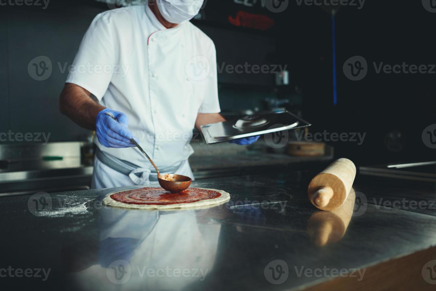 koch mit schützender coronavirus-gesichtsmaske, die pizza zubereitet foto