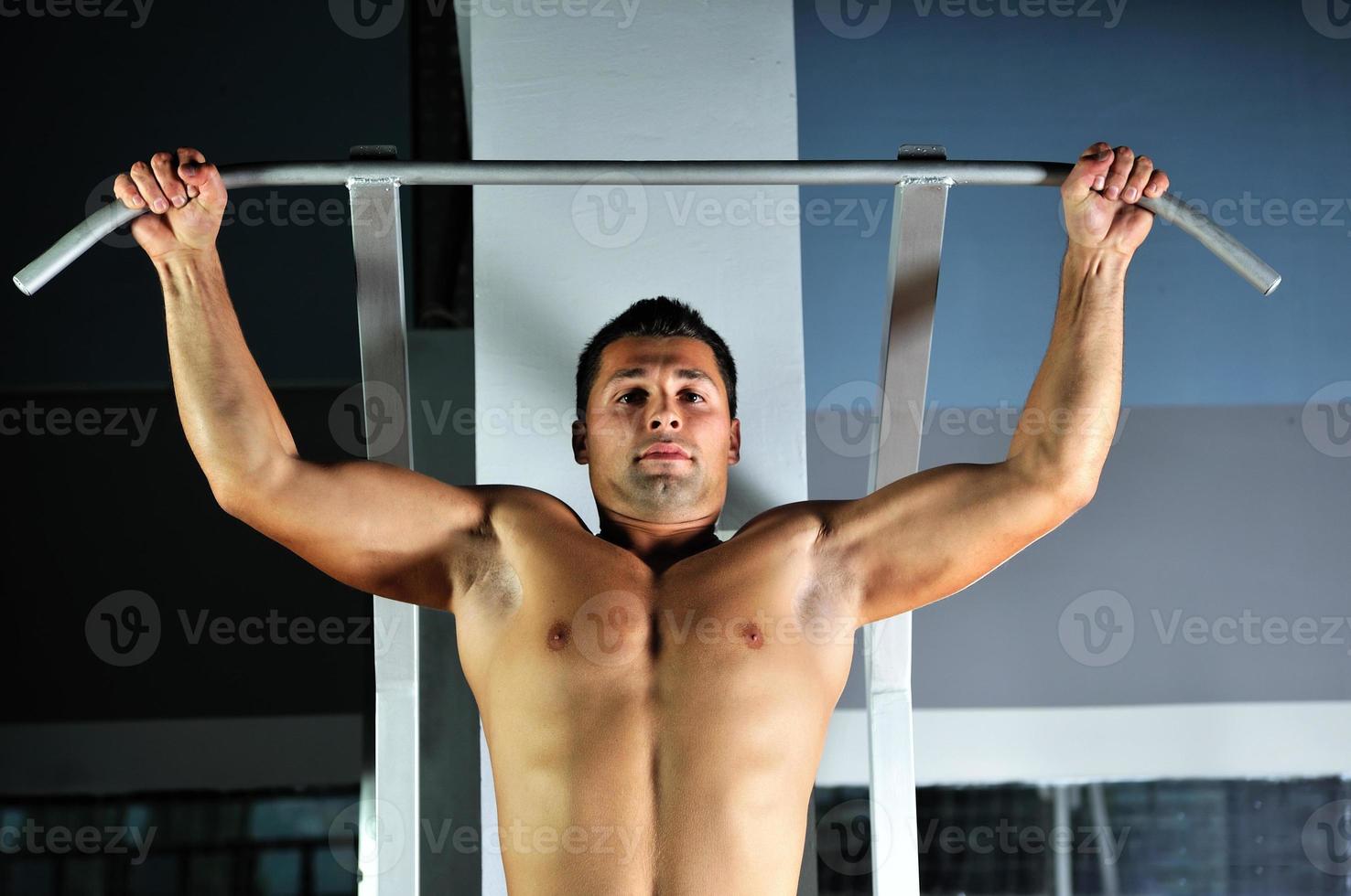 junger Mann mit starken Armen, der im Fitnessstudio trainiert foto