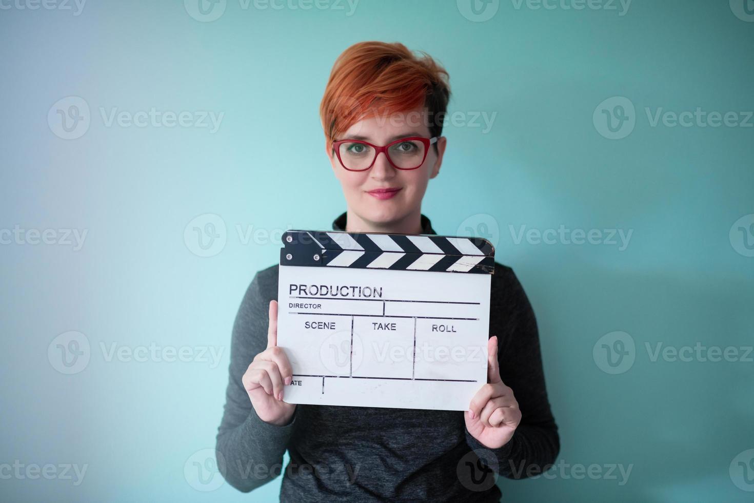 Rothaarige Frau mit Filmklöppel auf cyanfarbenem Hintergrund foto