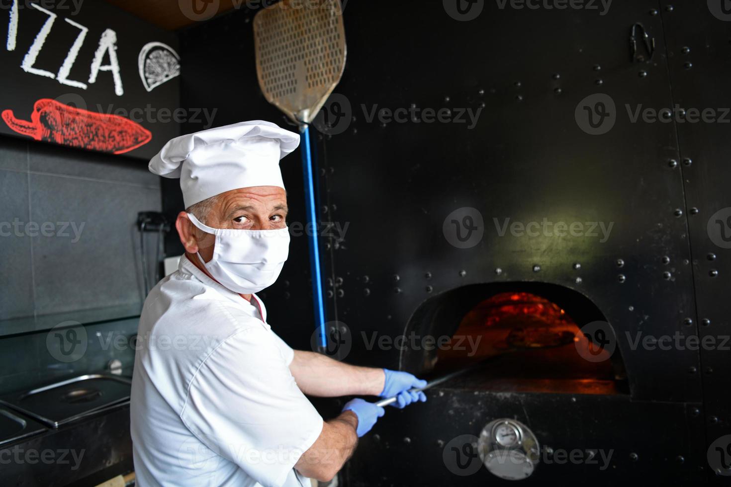 koch mit schützender coronavirus-gesichtsmaske, die pizza zubereitet foto