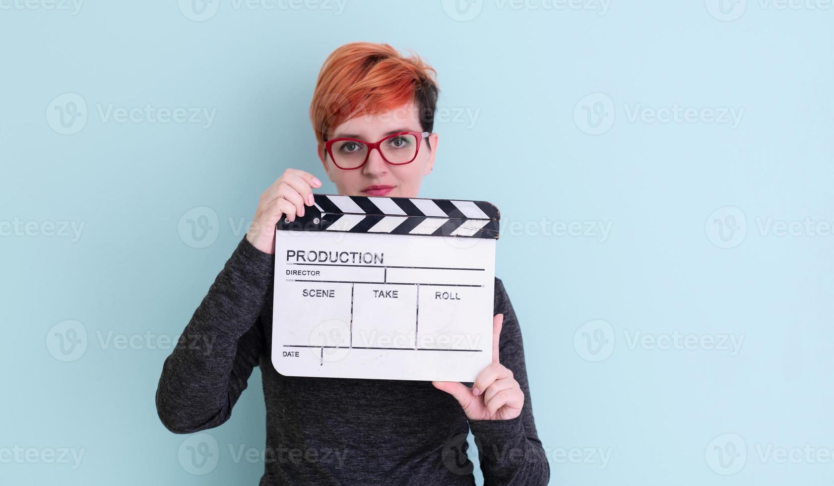 Rothaarige Frau mit Filmklöppel auf cyanfarbenem Hintergrund foto