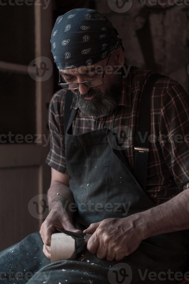 Löffelhandwerksmeister in seiner Werkstatt mit handgefertigten Holzprodukten und Werkzeugen arbeiten foto