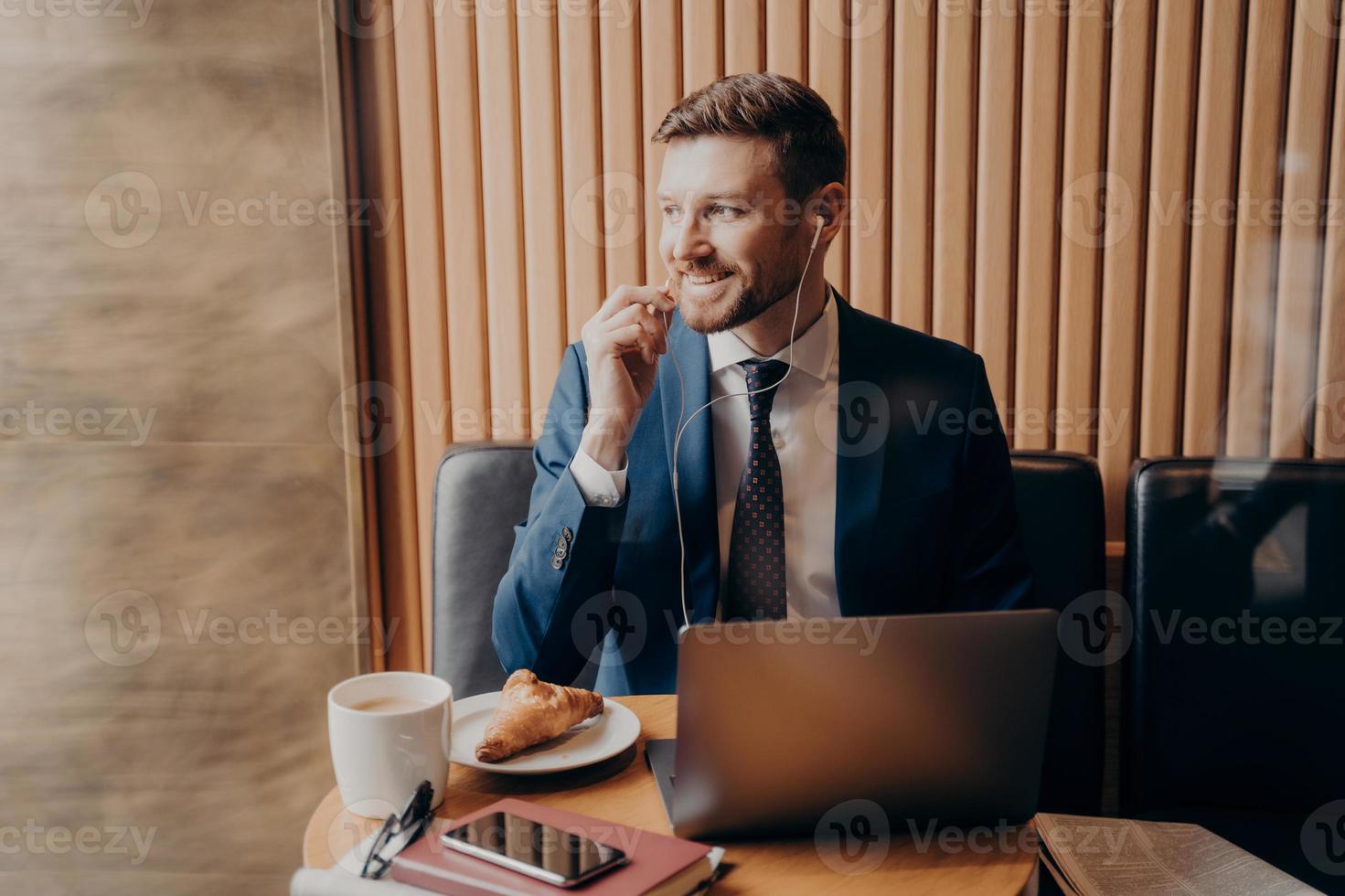 männlicher Investor im blauen Anzug, der online über Laptop im Restaurant mit Geschäftspartnern spricht foto