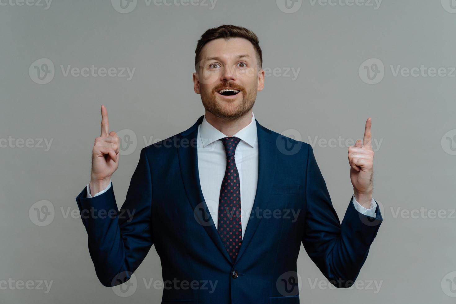 schockierter geschäftsmann im anzug, der mit den fingern nach oben zeigt und mit erstauntem gesichtsausdruck aussieht foto