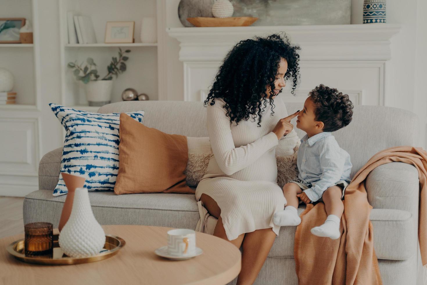 porträt der schönen familie schwangere mutter und sohn afroethnische rasse sitzen auf dem sofa foto