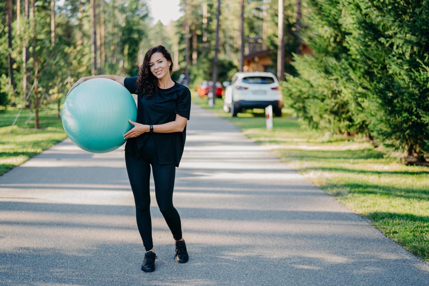 Ganzkörperaufnahme einer aktiven sportlichen Frau mit großen Fitnessballübungen Spaziergänge im Freien auf der Straße in der Nähe des Waldes führen zu einem gesunden Lebensstil und bleiben fit in Sportkleidung. Volksgymnastik und Aerobic foto