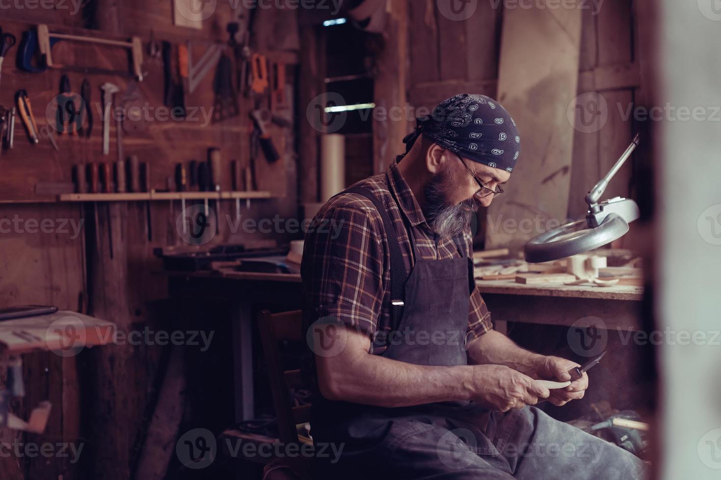 Löffelmeister in seiner Werkstatt mit Holzprodukten und Werkzeugen foto