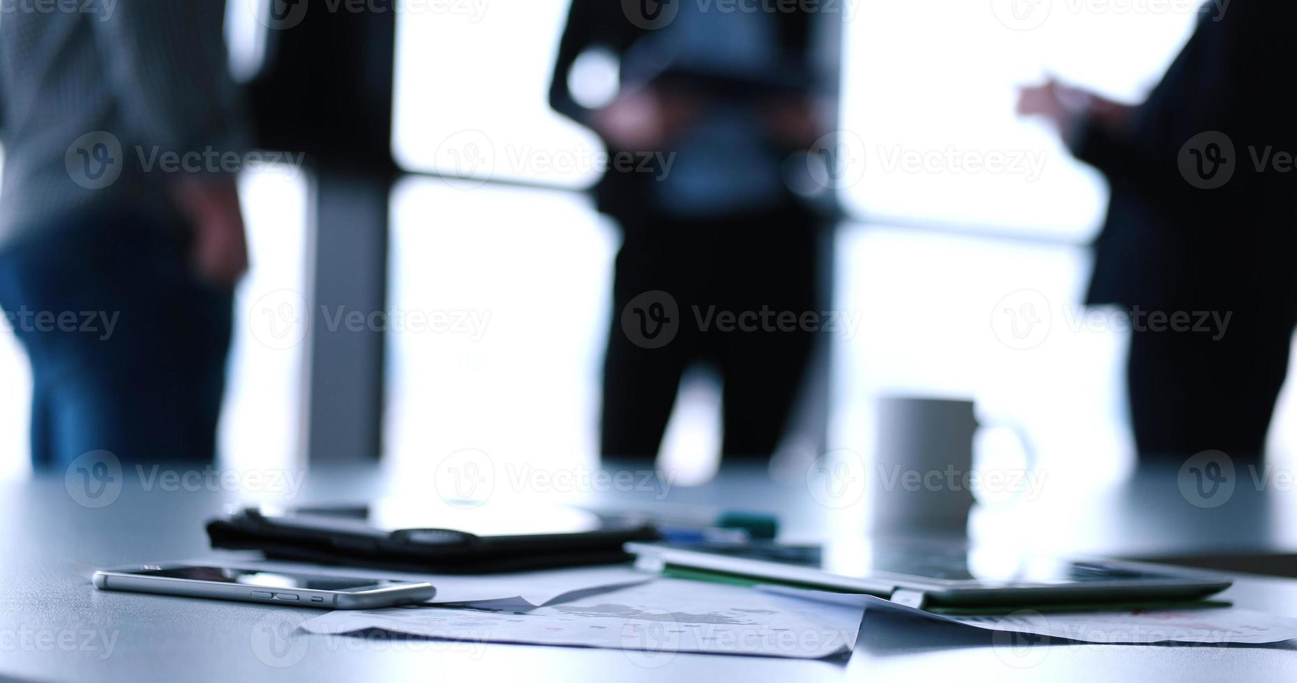 Tablet, Handy und Tasse Kaffee im Büro mit Geschäftsleuten im Hintergrund foto