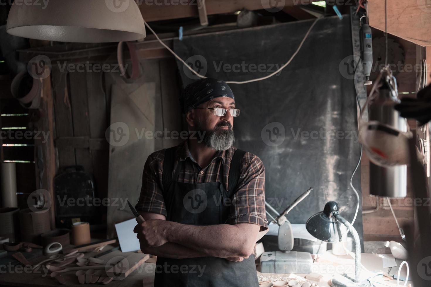 Löffelhandwerksmeister in seiner Werkstatt mit handgefertigten Holzprodukten und Werkzeugen foto