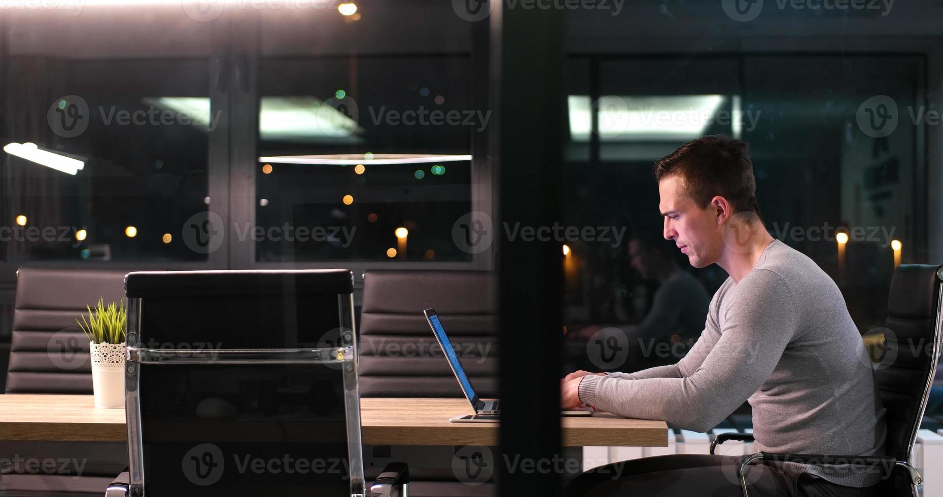 Mann, der im dunklen Büro am Laptop arbeitet foto