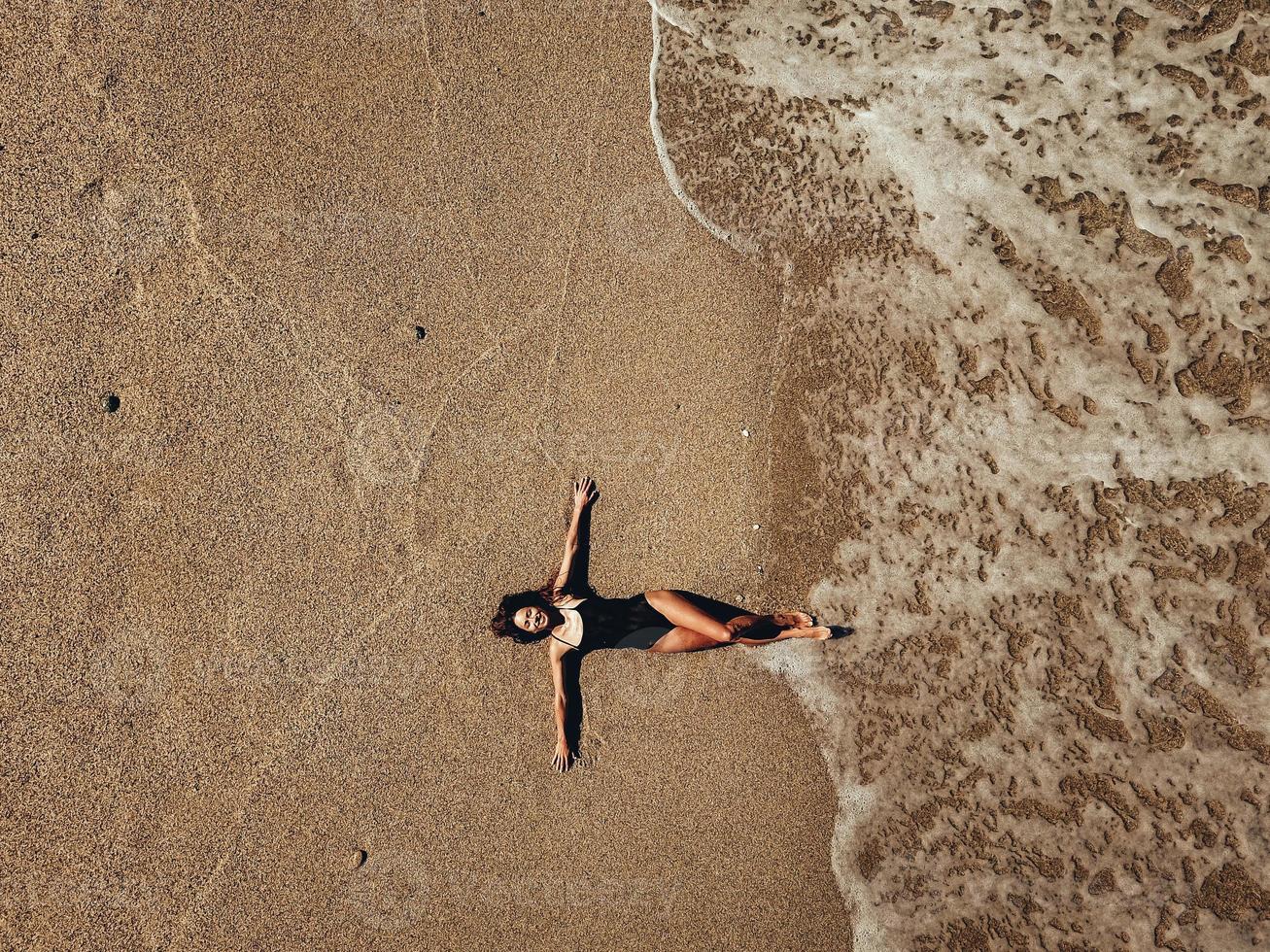 Luftdraufsicht junge Frau, die auf dem Sandstrand und den Wellen liegt foto