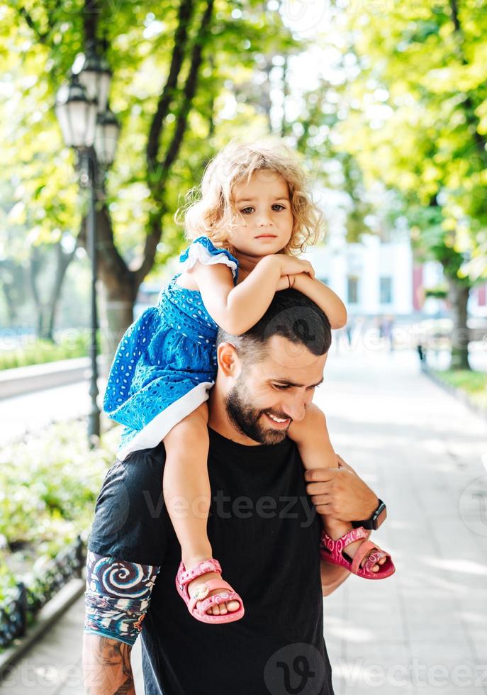 kleines Mädchen, das auf dem Hals des Vaters reitet foto