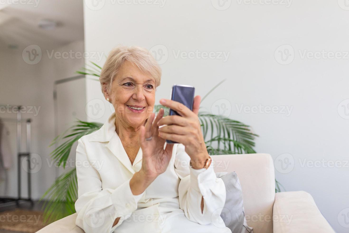 Reife Frau mit Handy an den Händen, die im Zimmer sitzt und Nachrichten an ihre Freunde und Familie sendet foto