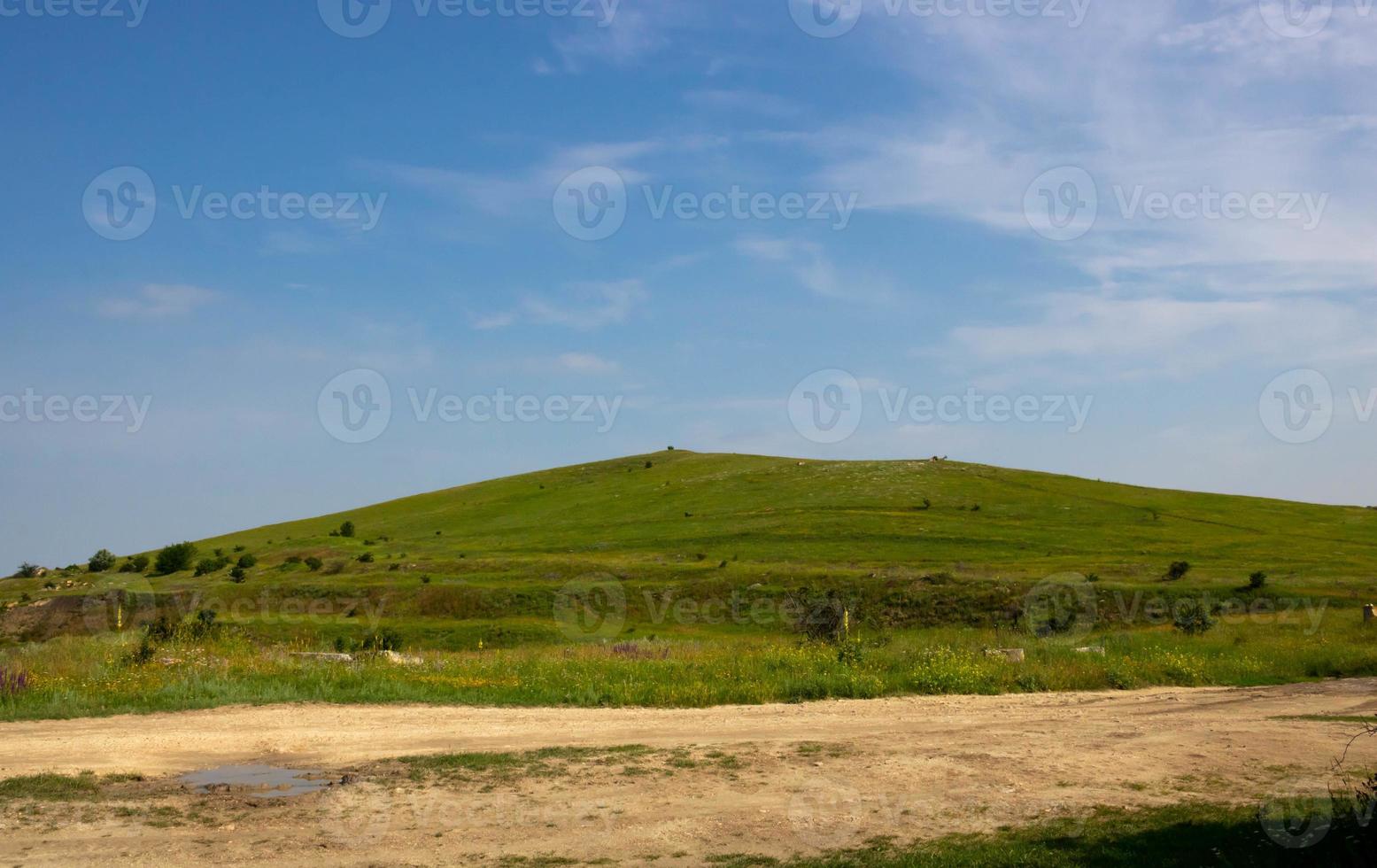 Ein grüner Hügel und eine unbefestigte Straße auf dem Hintergrund eines blauen Himmels mit Wolken foto