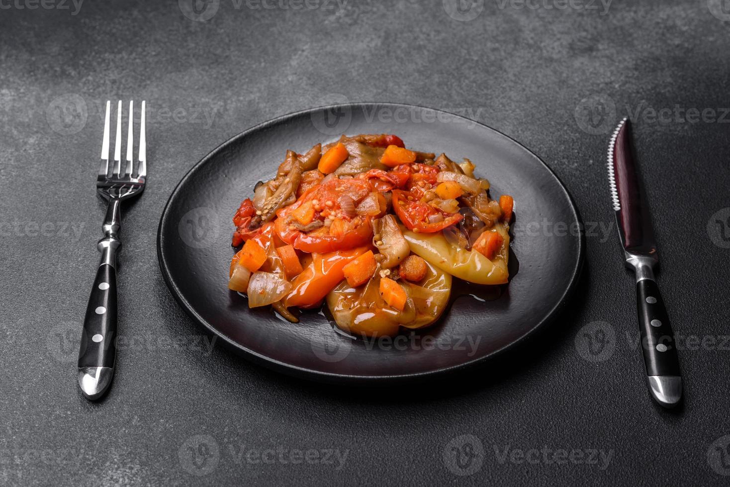 Gebackenes Gemüse, Auberginen, Paprika und Karotten auf einem schwarzen Teller auf Betongrund foto