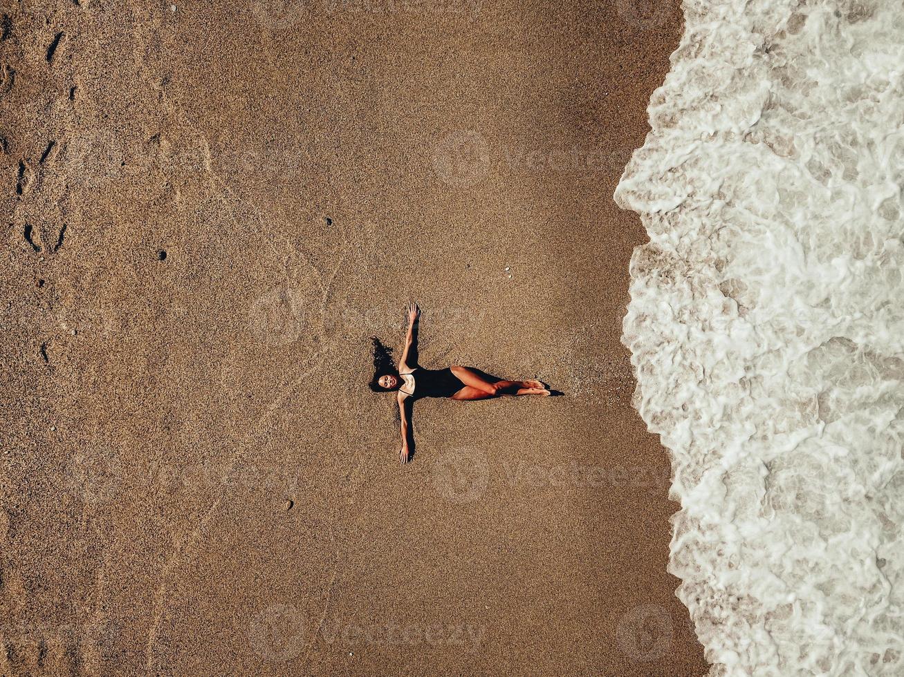 Luftdraufsicht junge Frau, die auf dem Sandstrand und den Wellen liegt foto