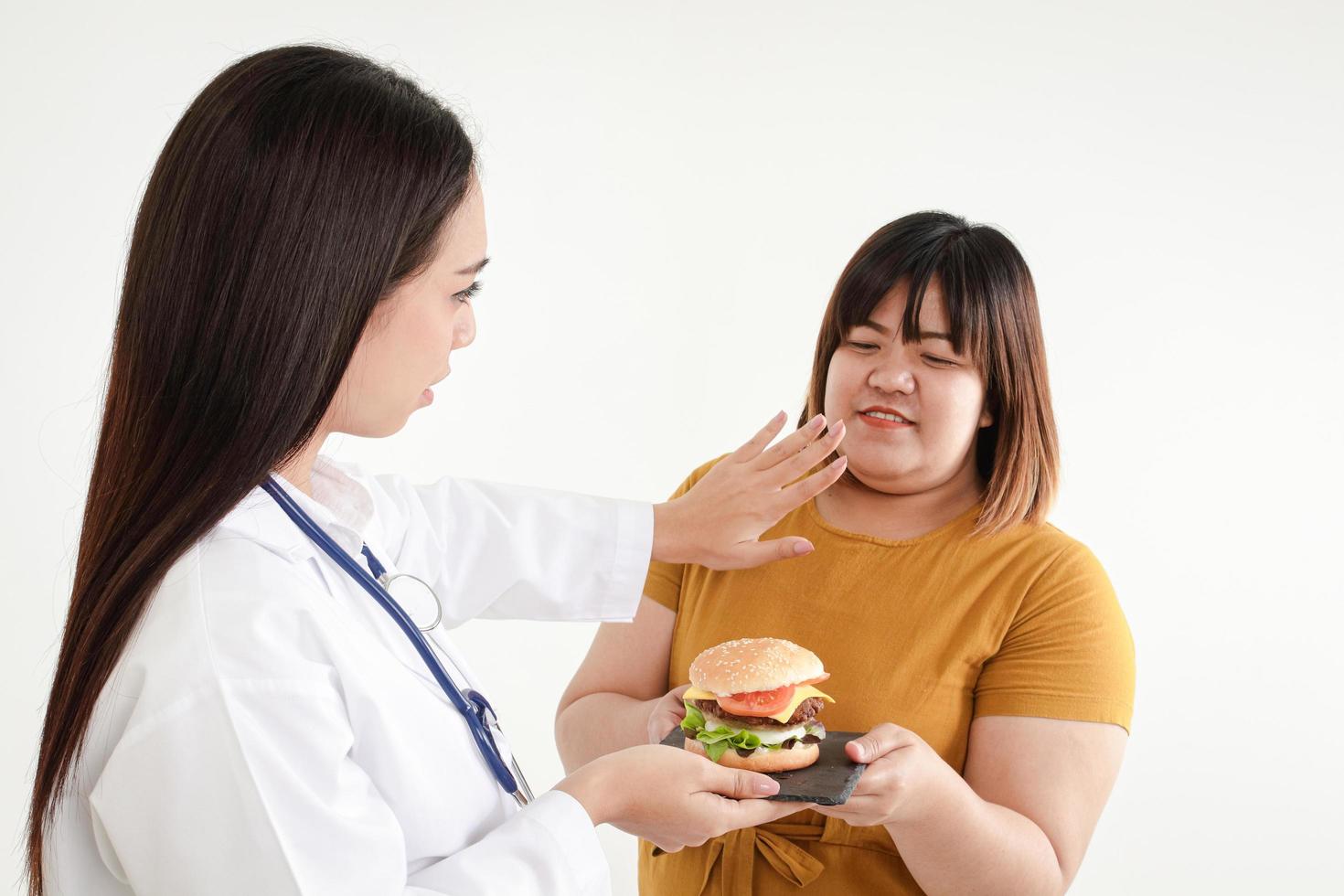 Eine Ärztin hält einen Hamburger für eine dicke Frau. weißer Hintergrund. Konzept der Gewichtskontrolle. diätetische Betreuung adipöser Patienten. gute Gesundheit zu haben foto