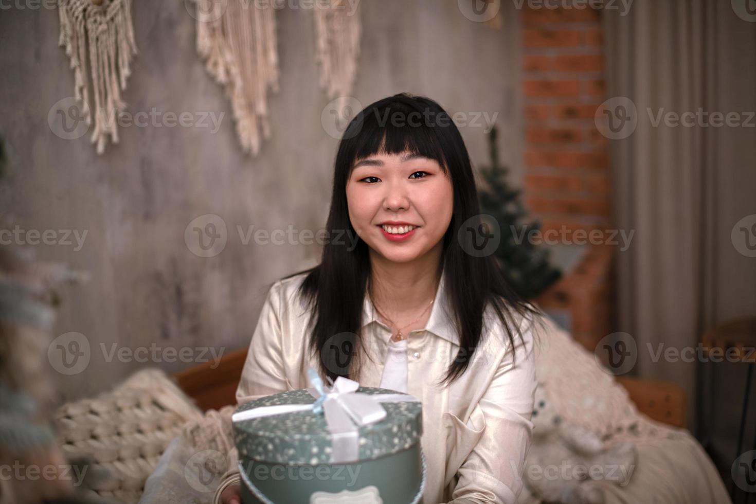 porträt einer schönen koreanischen jungen frau mit einem lächeln, das abends eine geschenkbox zu hause hält. foto