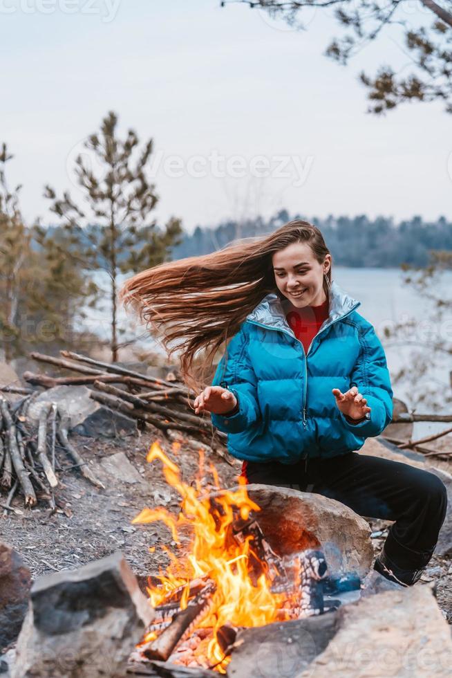 glückliches junges brünettes mädchen, das nahe bei lagerfeuer sitzt foto