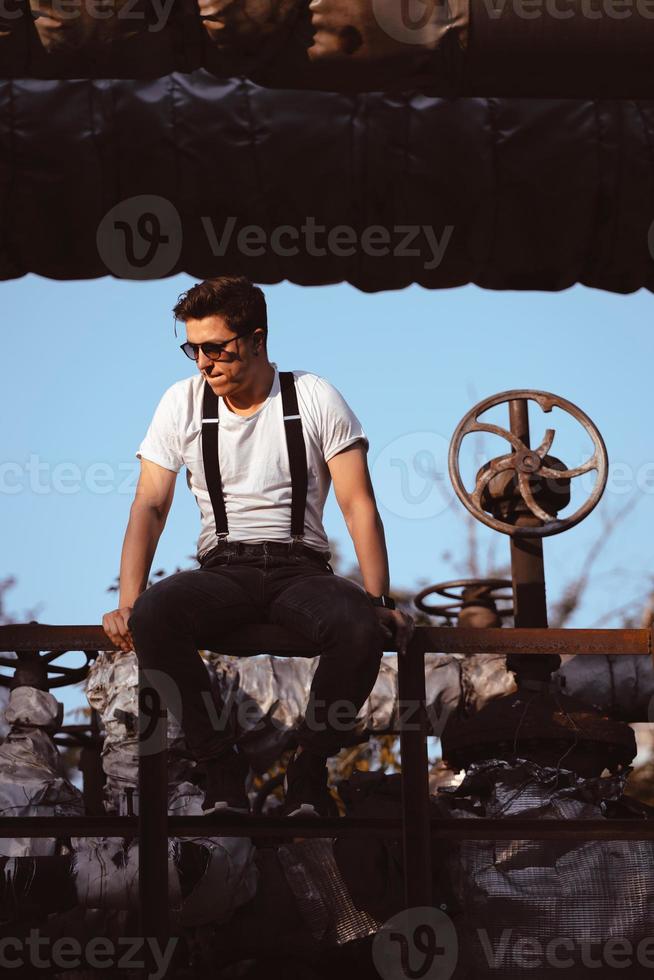 Typ in einem Hemd mit Hosenträgern, der an alten Rohren und Ventilen posiert foto