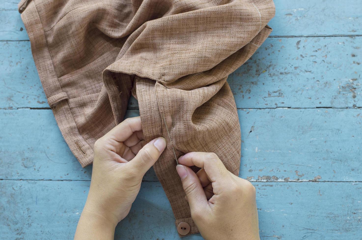 Draufsicht der Schneiderhand reparieren eine braune Hose auf blauem Tischhintergrund foto